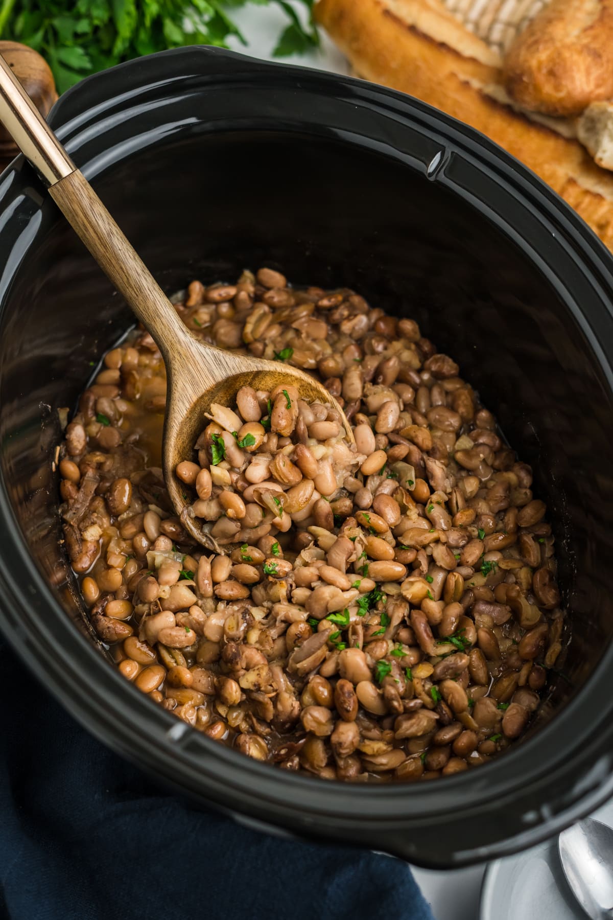 Pinto beans in the slow cooker with a wooden spoon lifting some up.