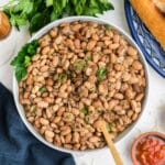 Crockpot pinto beans served up in a white bowl with some parsley sprinkled on top.