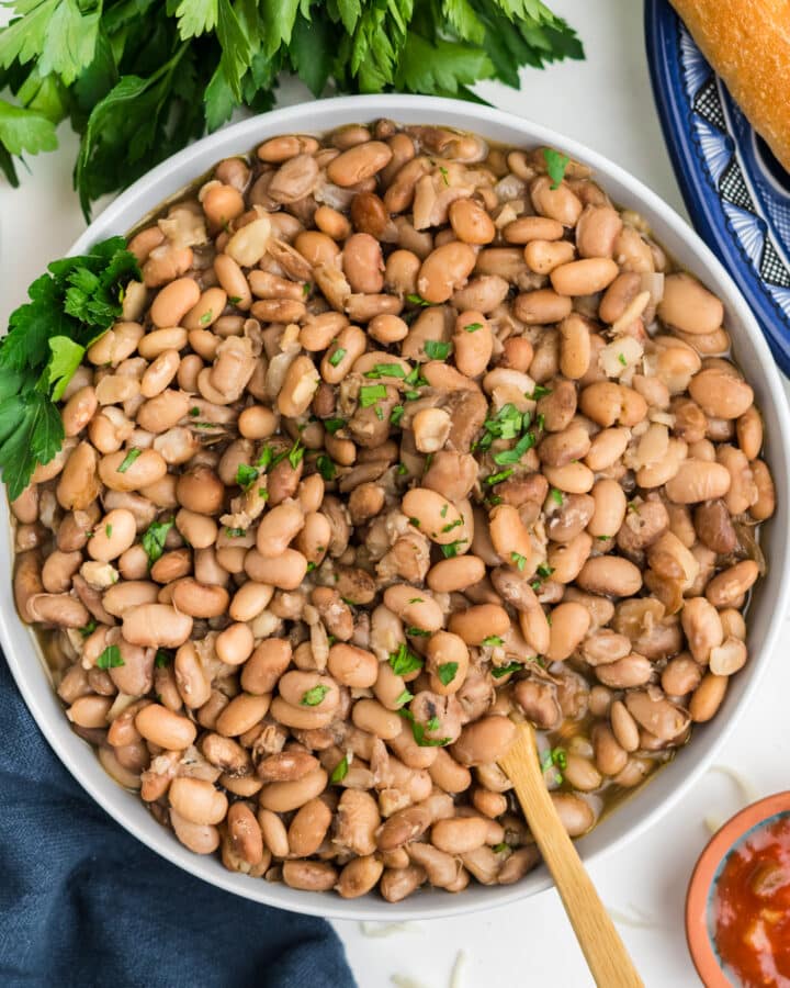 Crockpot pinto beans served up in a white bowl with some parsley sprinkled on top.
