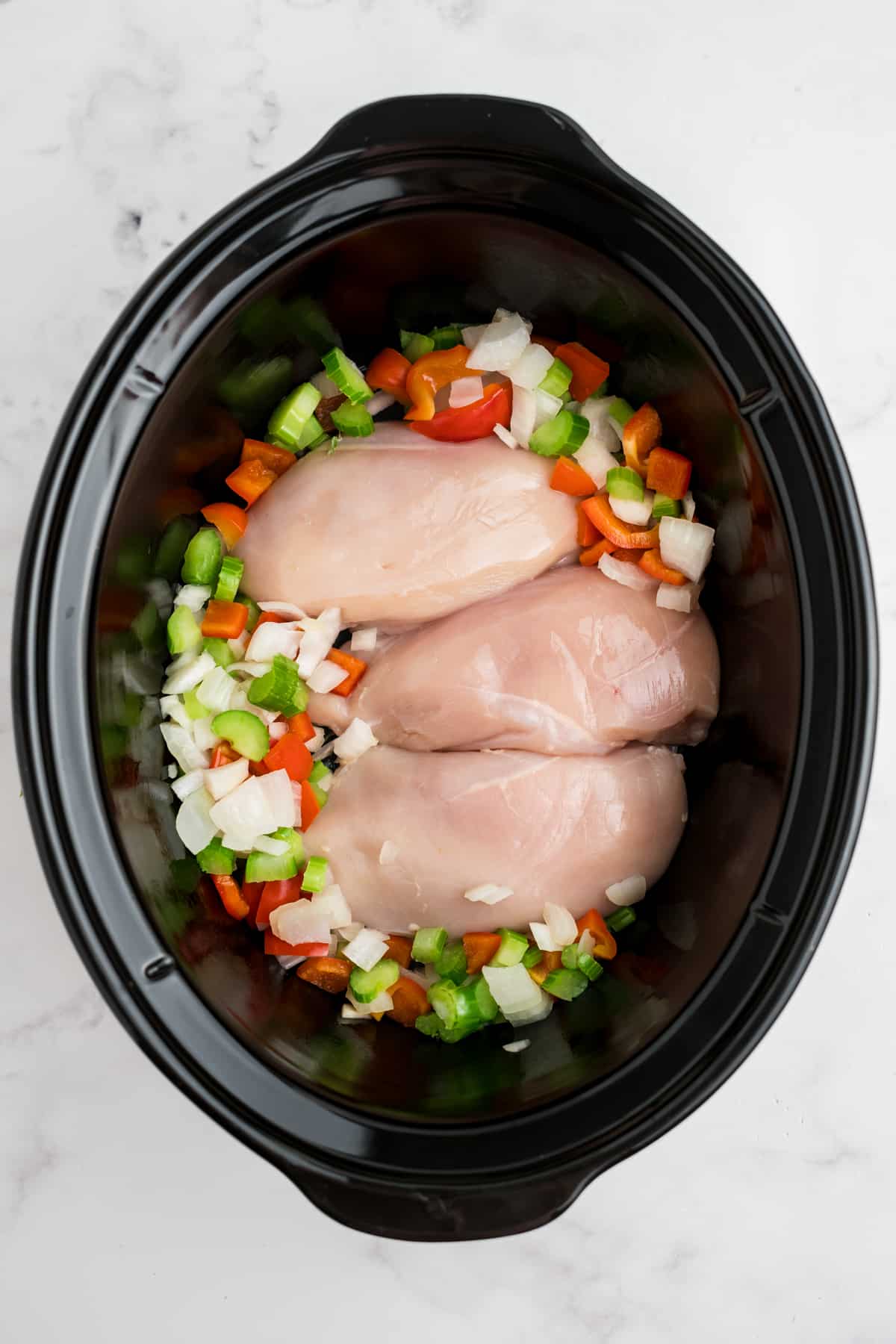 Raw chicken breasts and chopped veggies in a slow cooker.