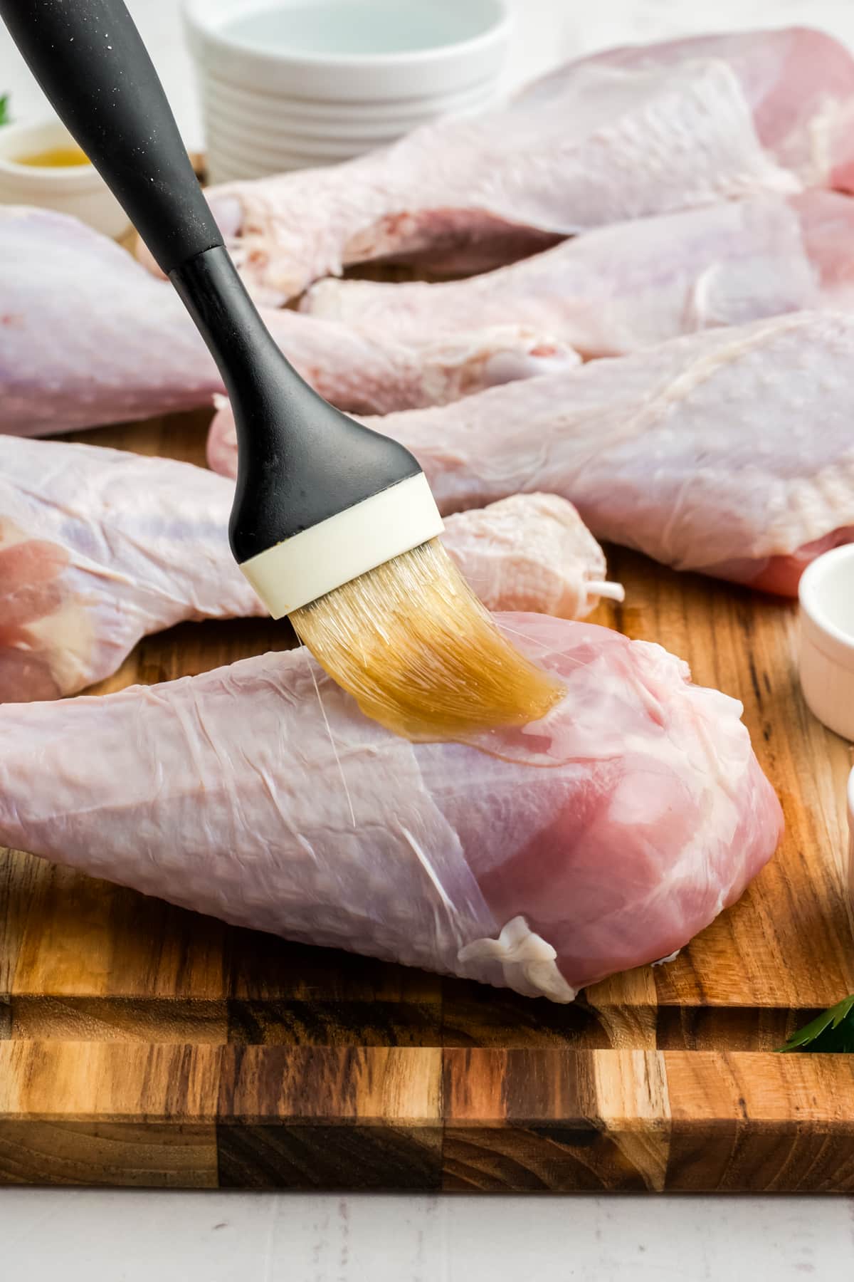Raw turkey legs being brushed with olive oil.