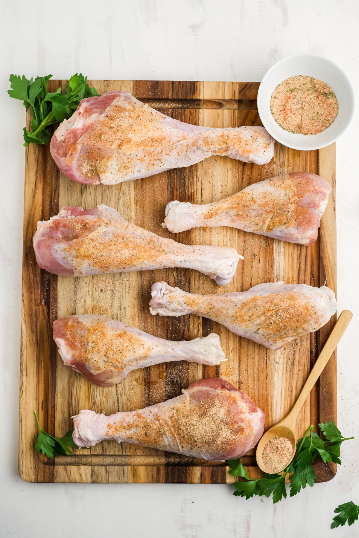 Seasoned raw turkey legs on a wooden cutting board.