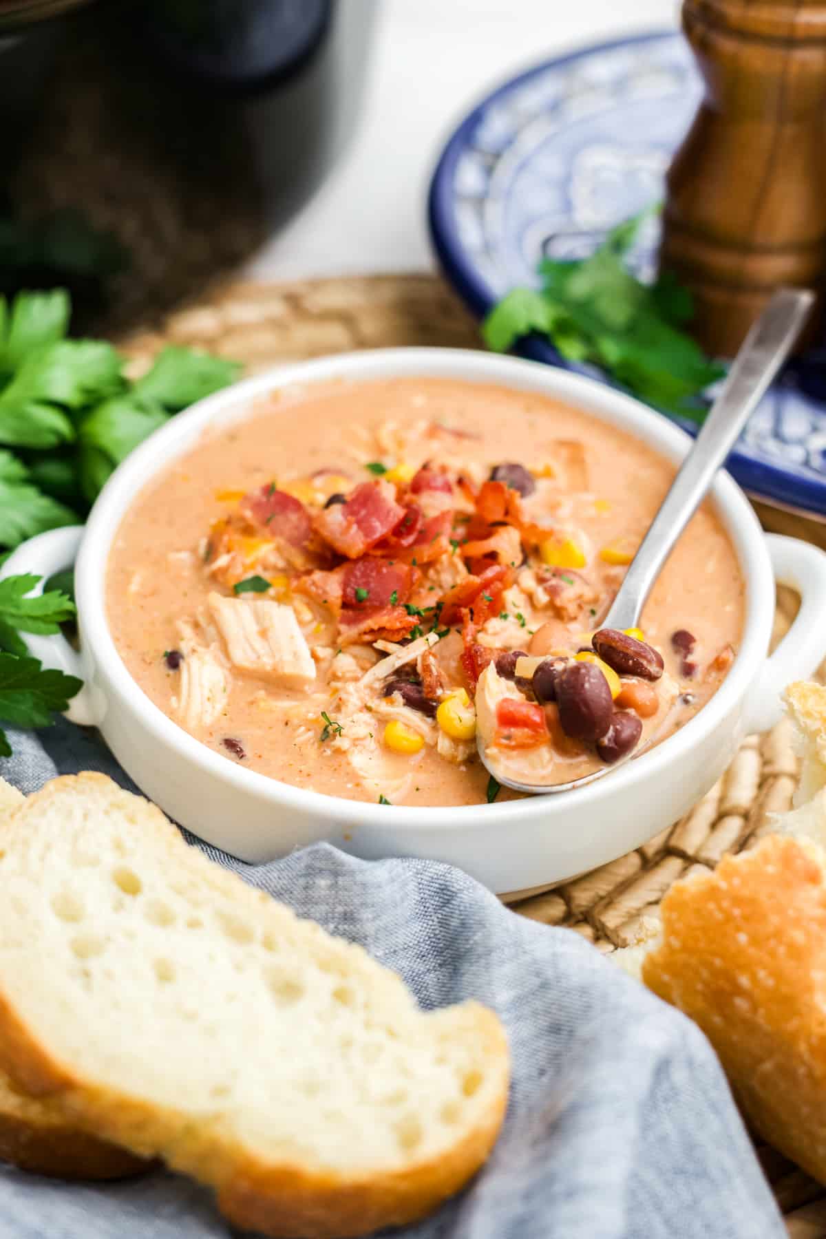 Crack chicken chili in a pot garnished with bacon and a spoonful resting on the side. 