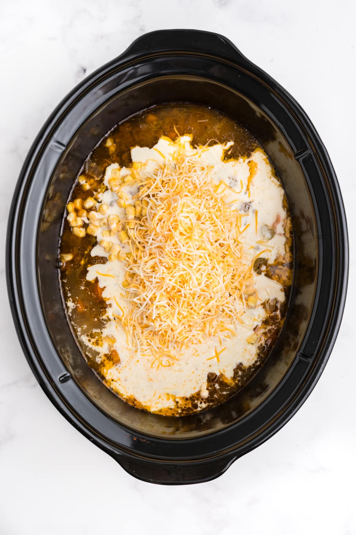 Corn, cream, and cheese added to the soup in the slow cooker.