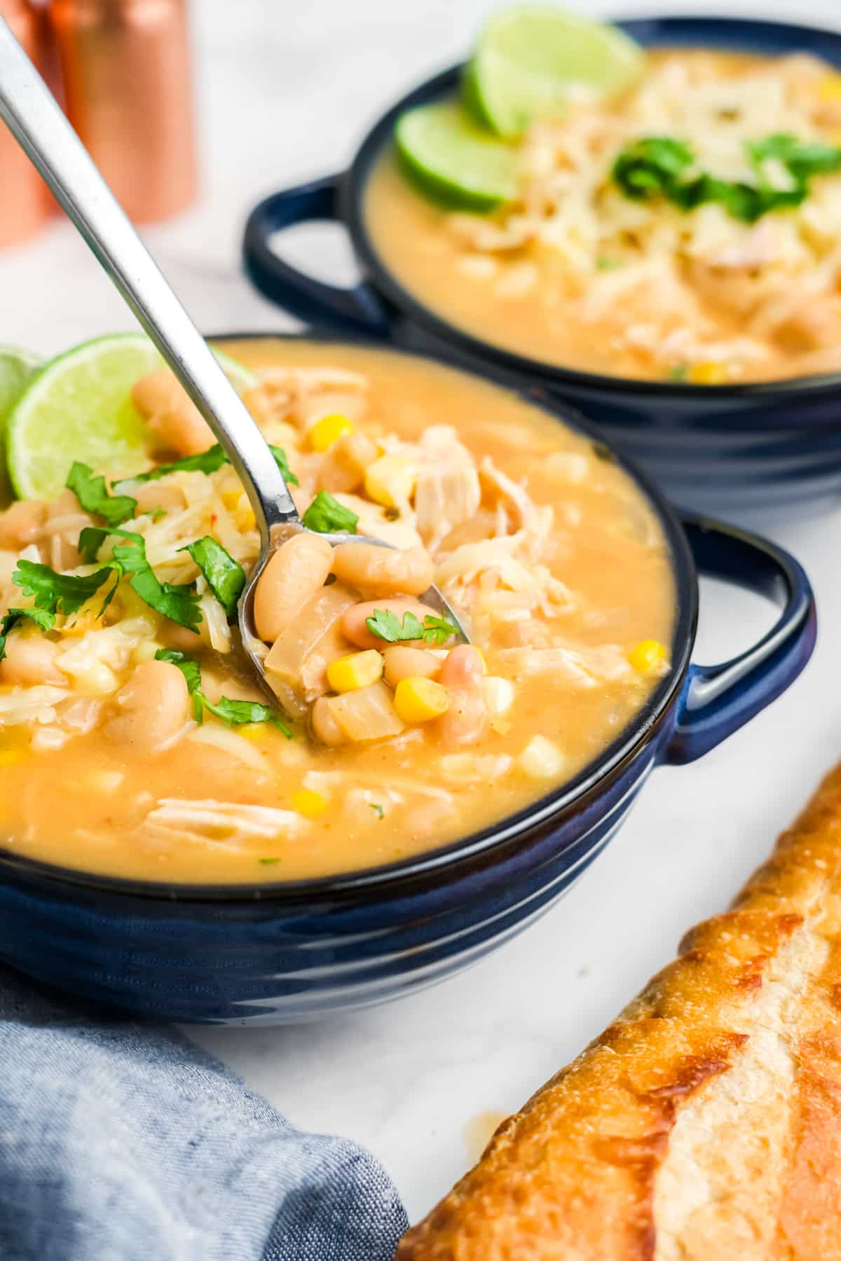 White chicken chili with corn in a bowl with a spoon lifting up a spoonful.