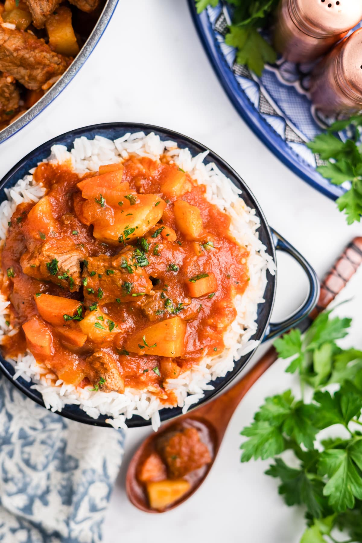 Hawaiian beef stew in a bowl next to a wooden spoon holding a bit and the pot with more in it. 