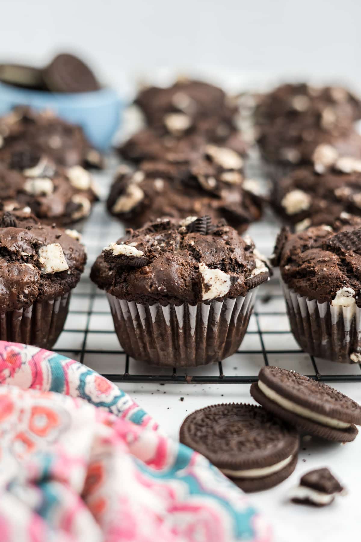 Oreo muffins on a cooling rack with two whole Oreo cookies resting on the table in front. 