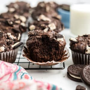 Oreo muffins on a cooling rack and the one in the front has the wrapper off and a bite taken.