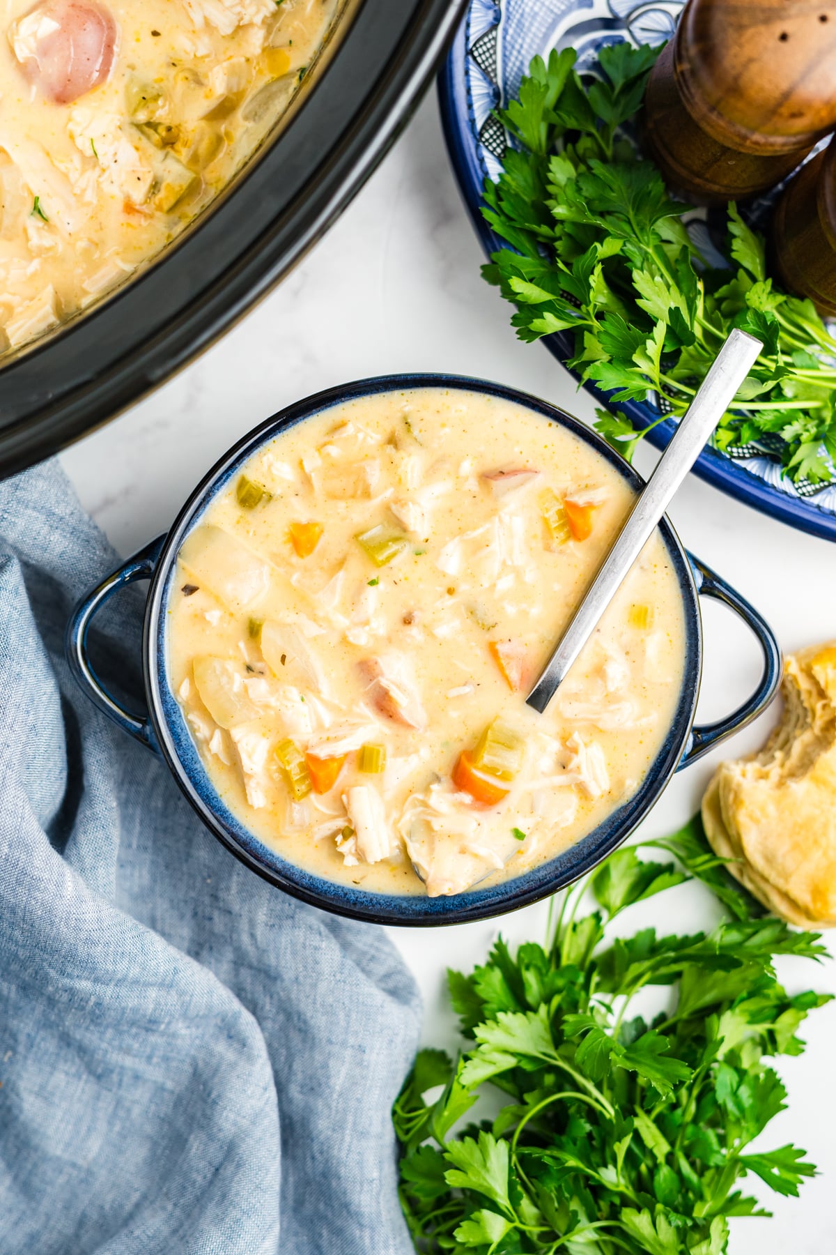 A blue soup bowl of slow cooker chicken stew with a spoon resting in the bowl.