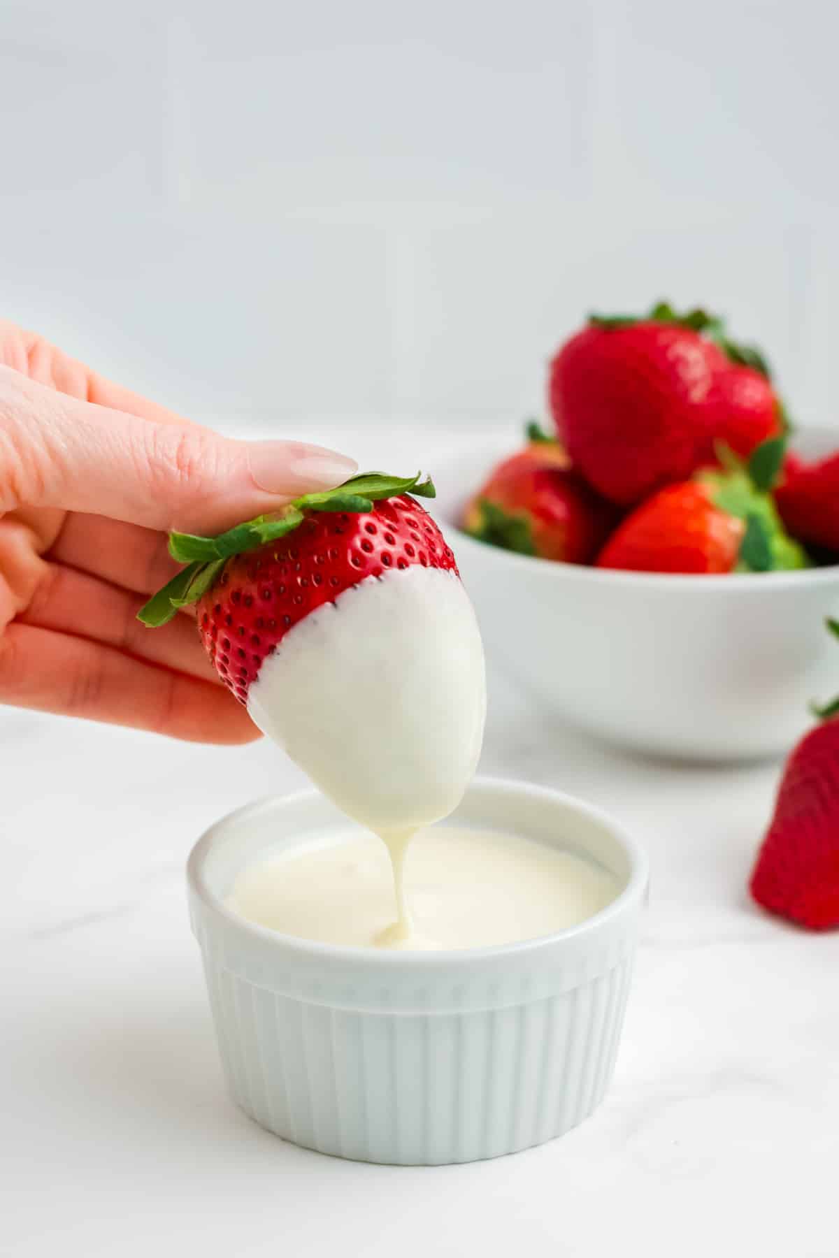 A strawberry dripping white chocolate after being dipped. 