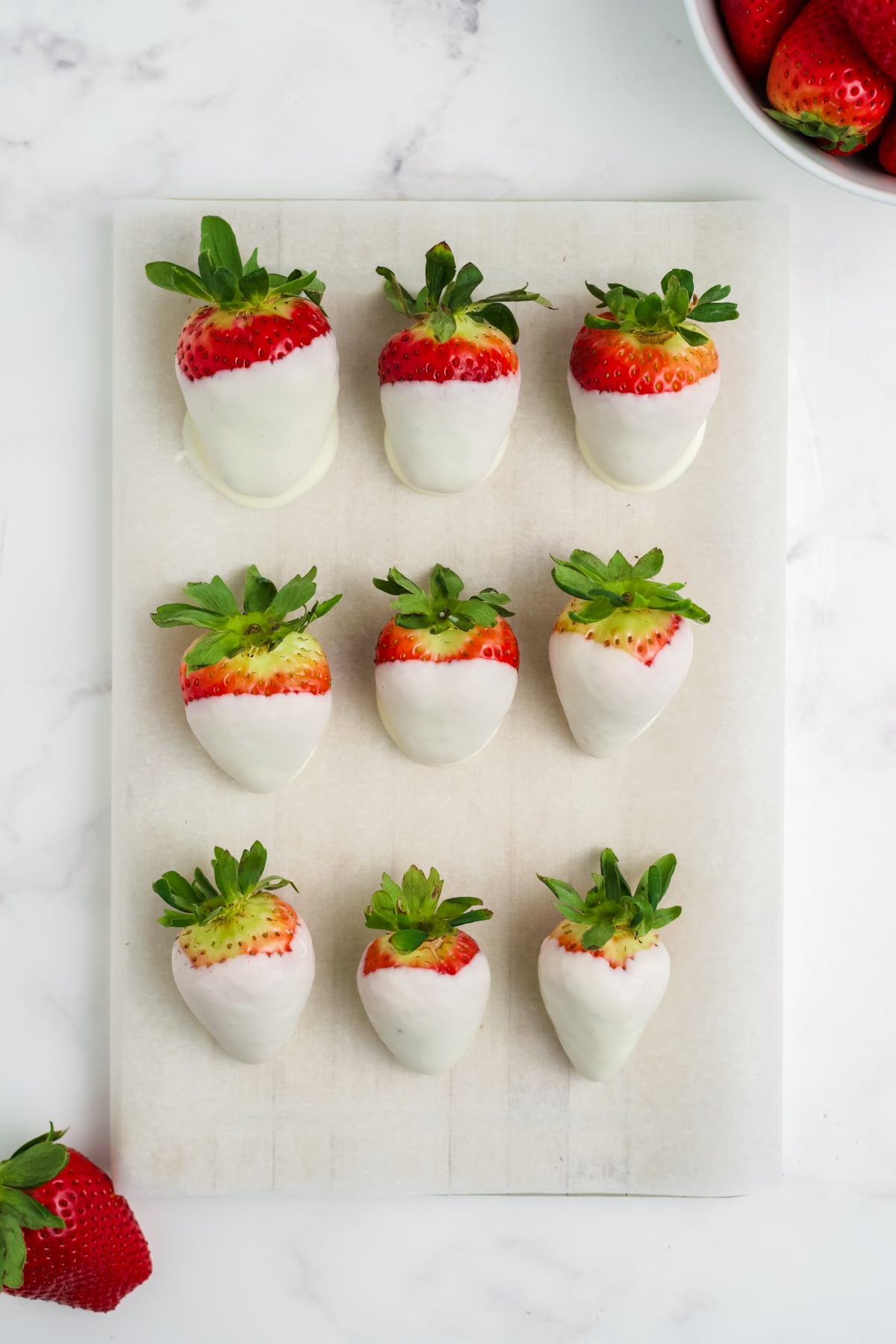An overhead image of 9 white chocolate strawberries on parchment paper.