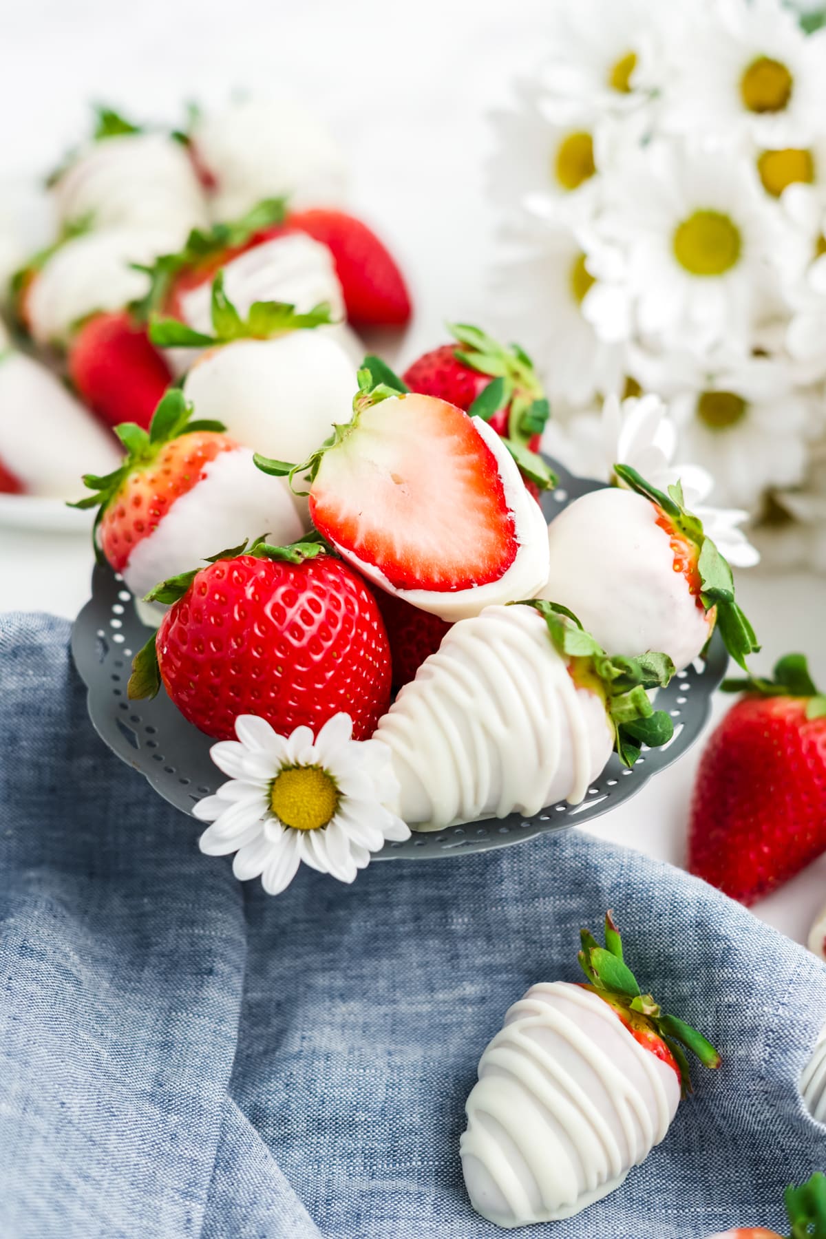 A stack of white chocolate covered strawberries on a little platter with one strawberry cut in half. 