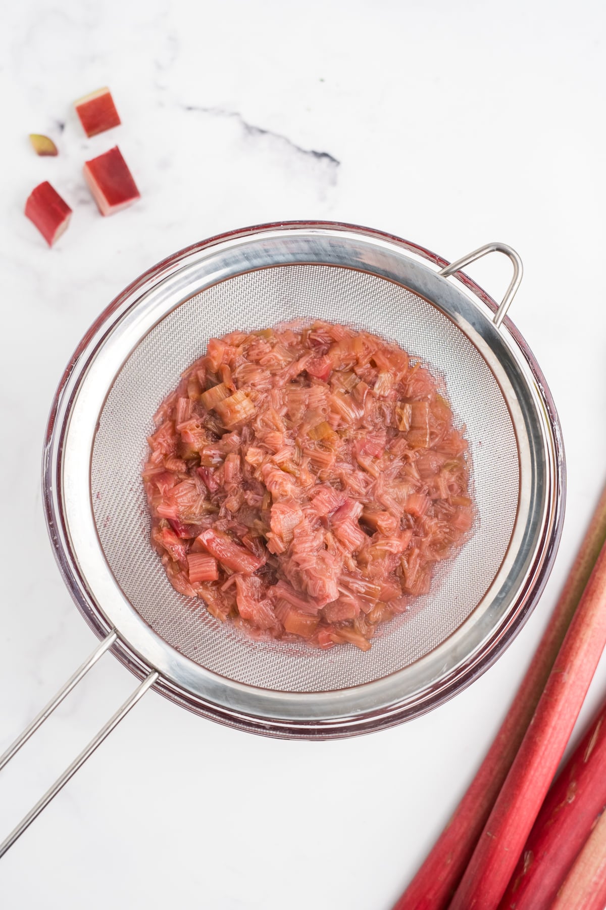 An overhead image of rhubarb being strained from simple syrup.
