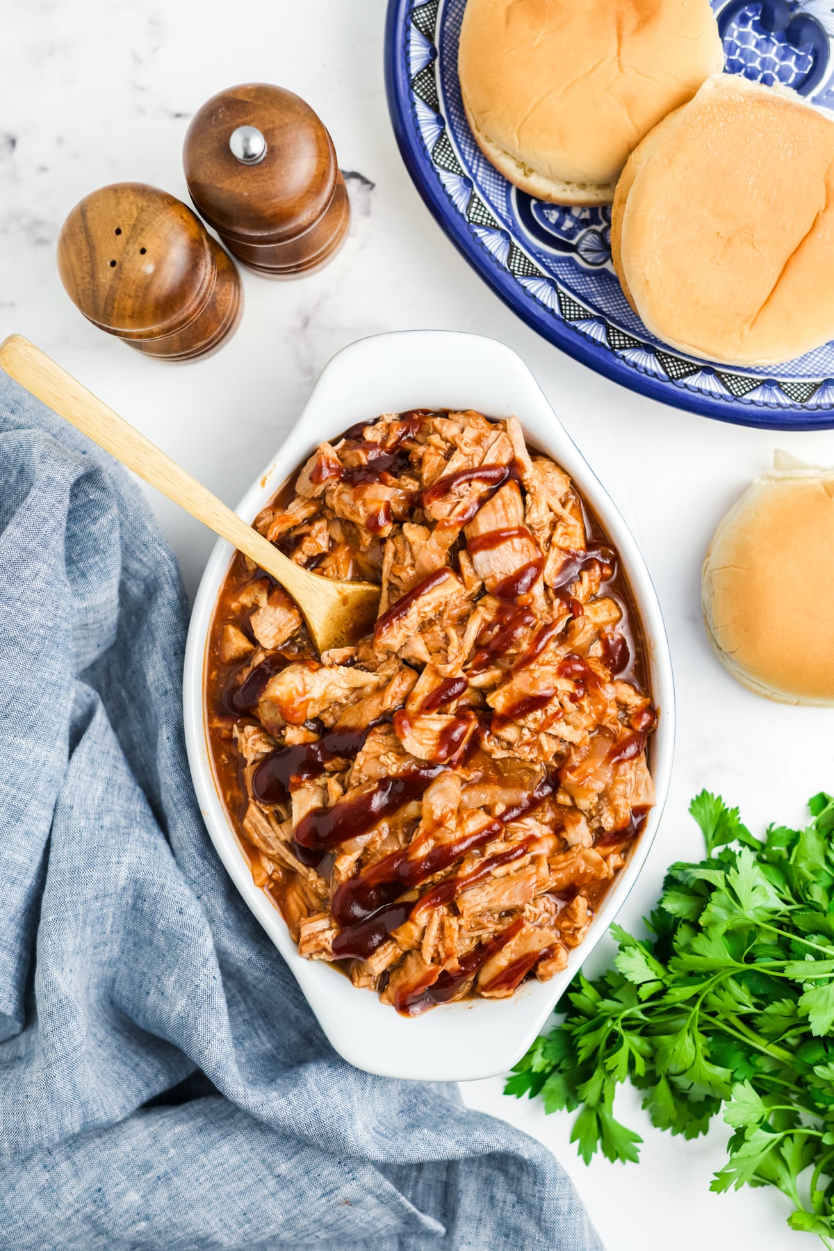 Pulled pork tenderloin in a serving dish with a wooden spoon resting in the dish.
