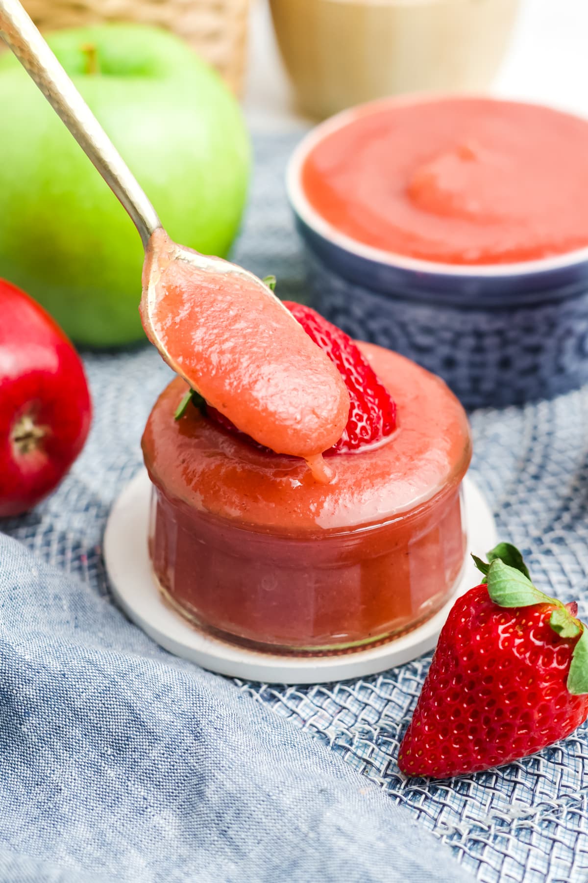 A spoon holding up a portion of homemade strawberry applesauce over a dish of more. 