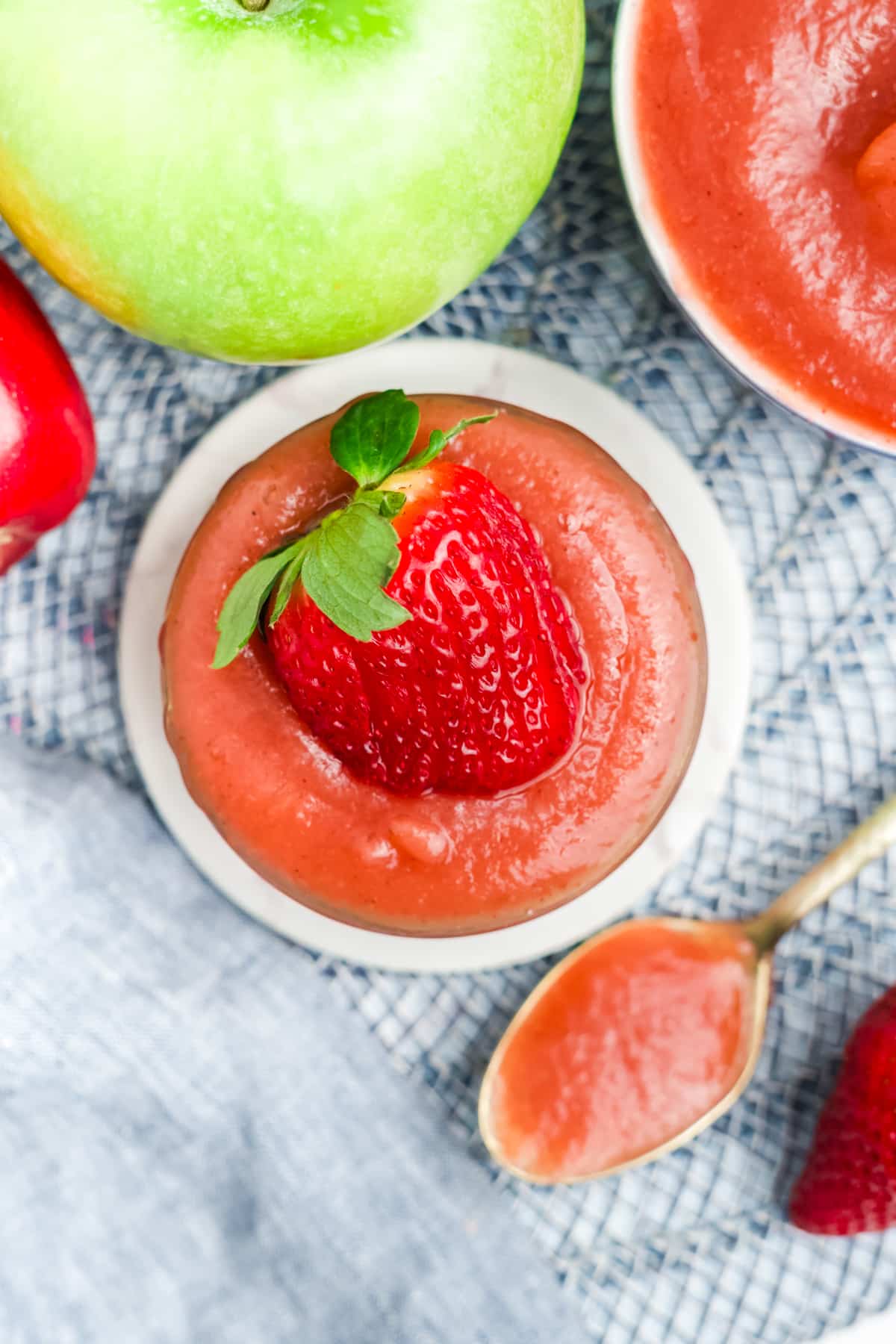 Strawberry applesauce in a dish surrounded by a spoonful and fresh berries and apples.