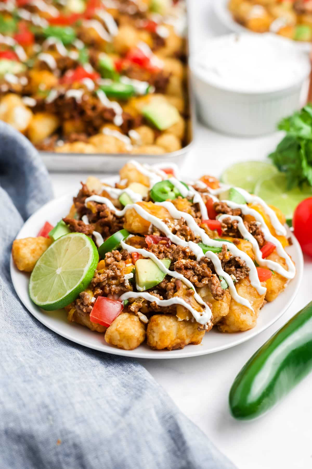 Totchos on a plate drizzled with sour cream and garnished with lime. 