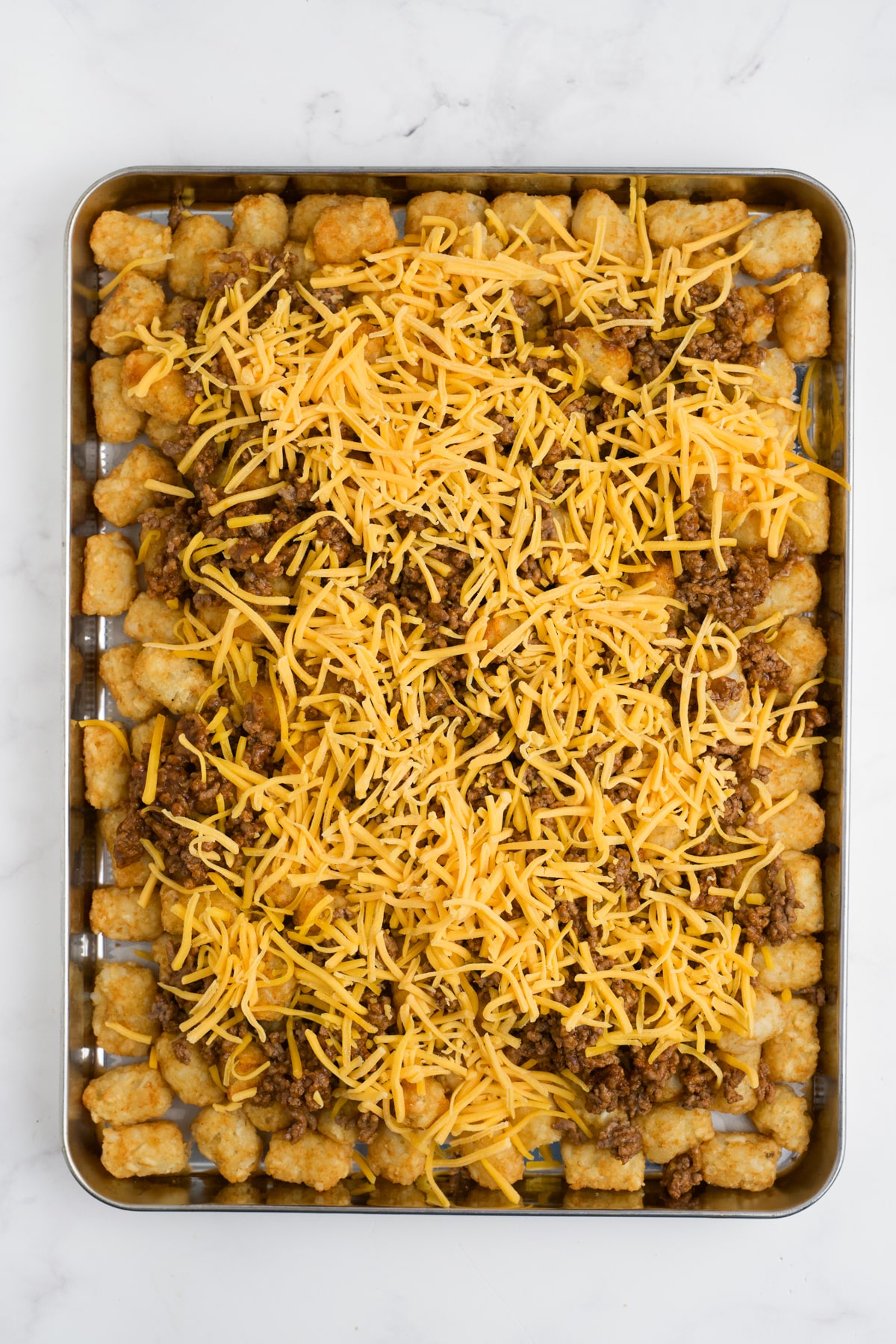 Meat an cheese added to tater tots on a pan.