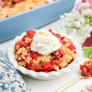 A dish of rhubarb dump cake topped with whipped cream in front of the pan of more.