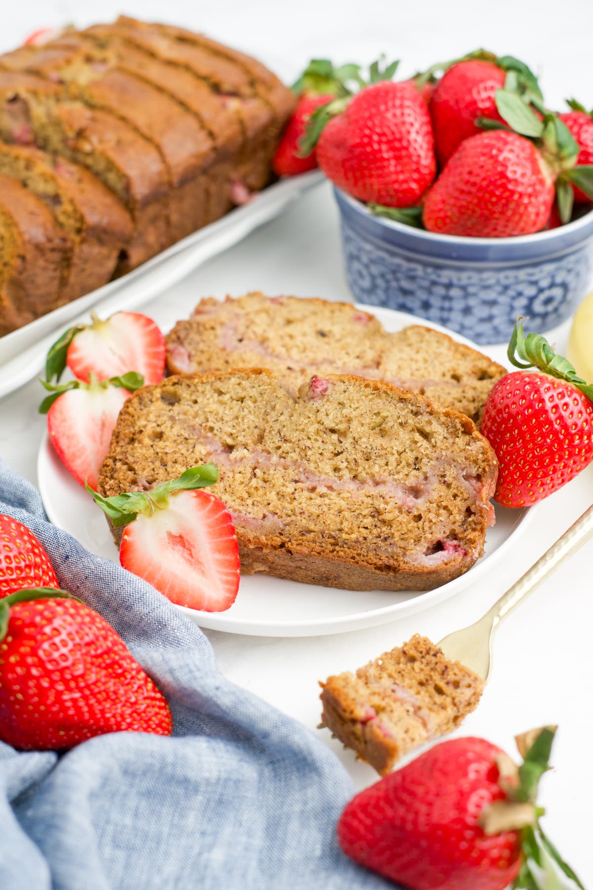 Slices of strawberry banana bread on a plate with a bowl of strawberries to the side. 