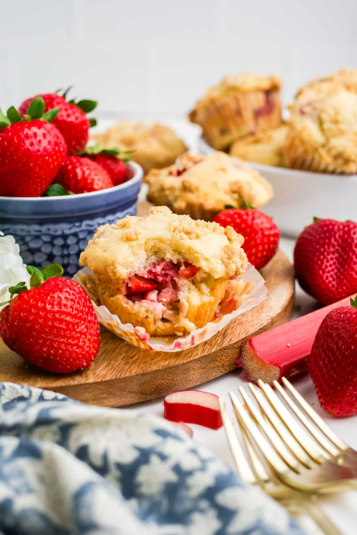 Strawberry rhubarb muffin with a bite missing in front of a bowl of berries. 