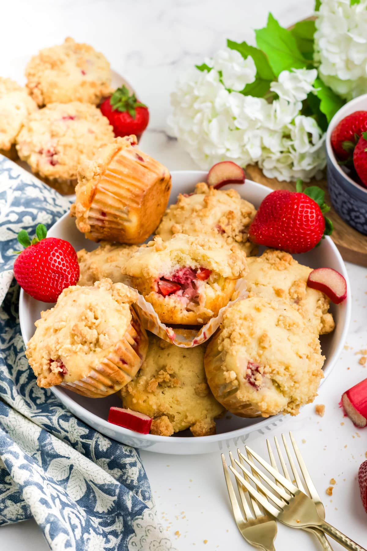 Strawberry rhubarb muffins in a bowl with a bite missing from the one on top.