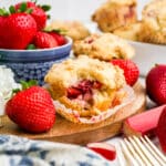 Strawberry rhubarb muffins on a table with a bowl of strawberries.