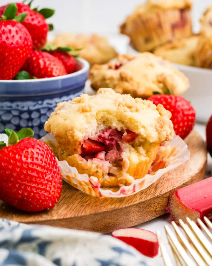 Strawberry rhubarb muffins on a table with a bowl of strawberries.