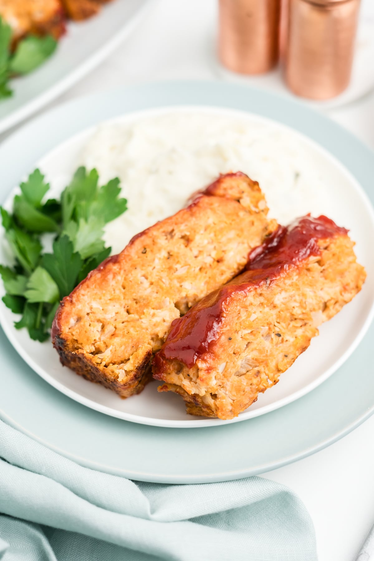 Two slices of chicken meatloaf with a glaze on the top on a plate and garnished with fresh parsley.