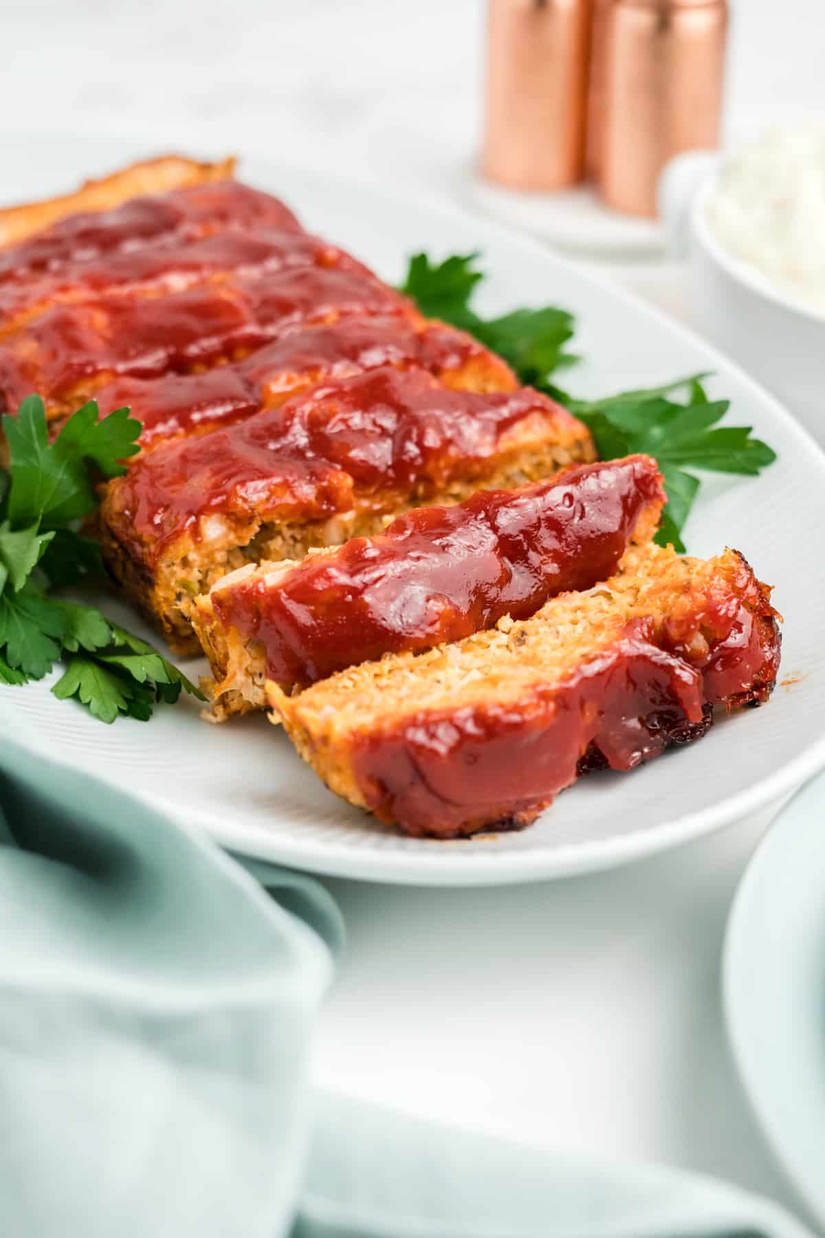 Slices of chicken meatloaf on a white oval platterwith ketchup sauce on top.