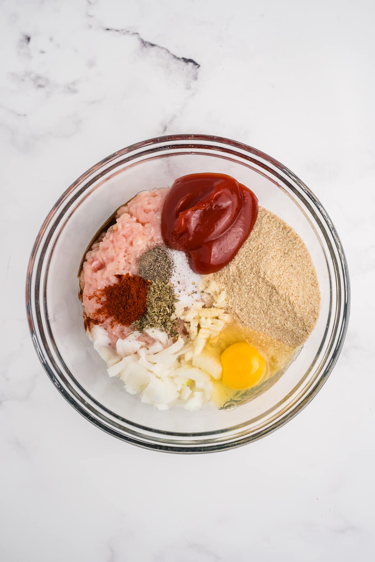 Chicken, onions, eggs, spices, breadcrumbs and ketchup in a bowl.