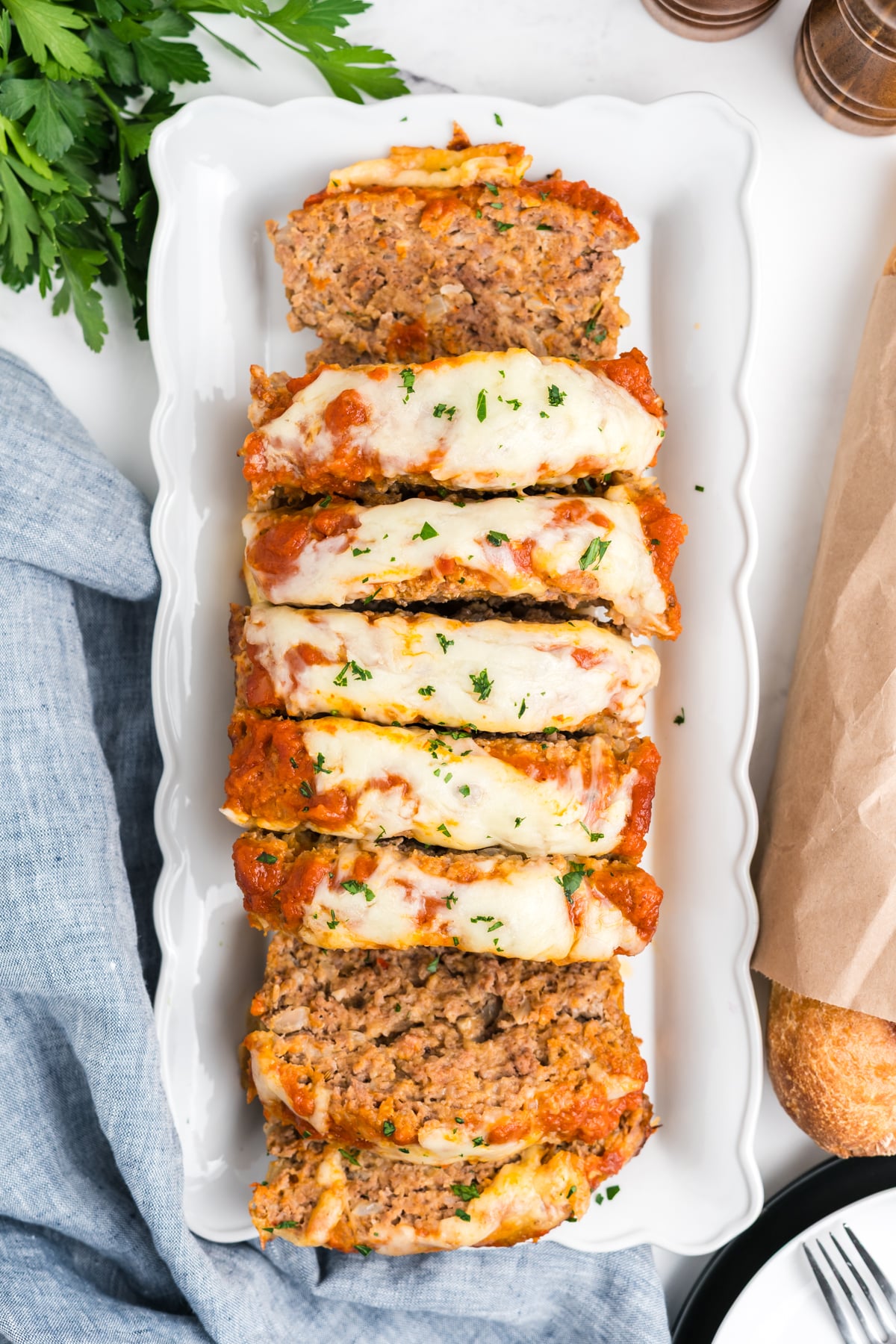 Italian meatloaf sliced up on a platter and topped with sauce and mozzarella cheese. 