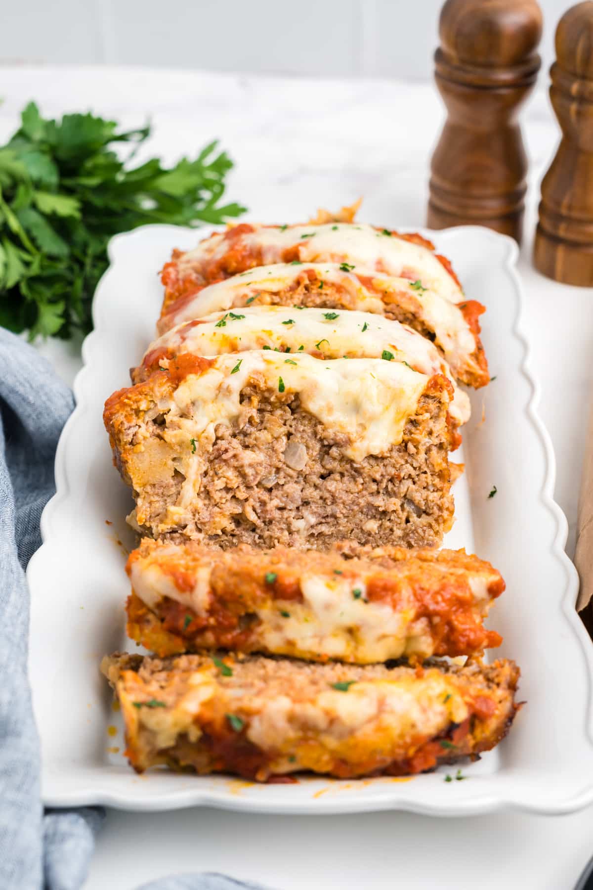 Italian meatloaf with cheese on top sliced on a white platter. 