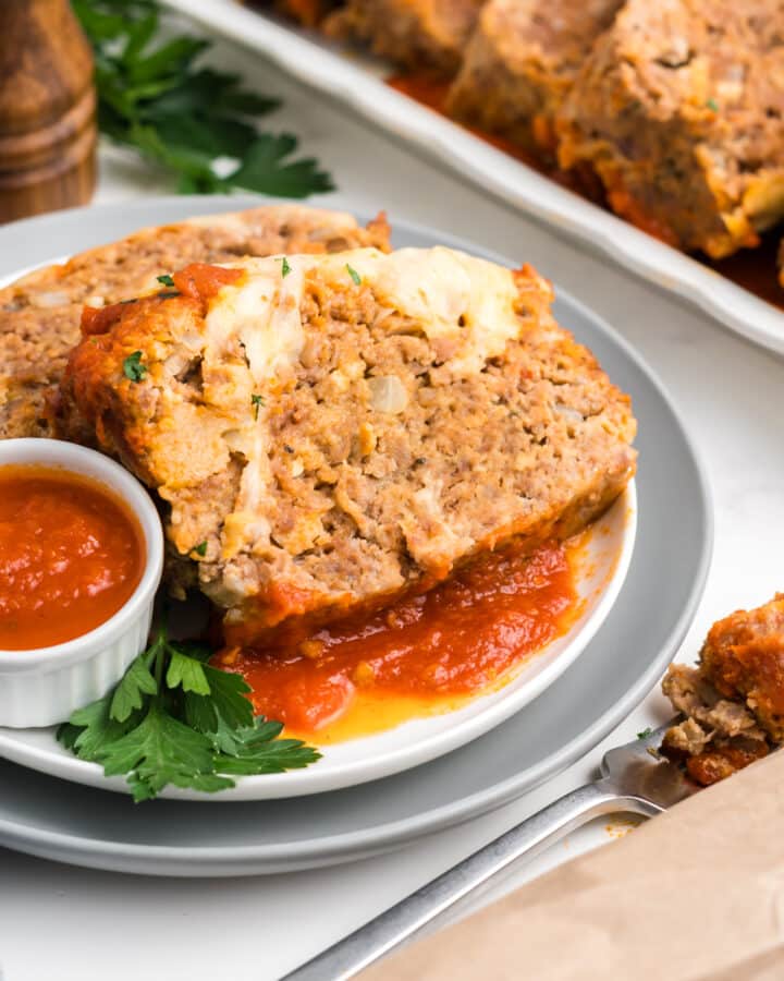 A plate of Italian meatloaf with a side of sauce.