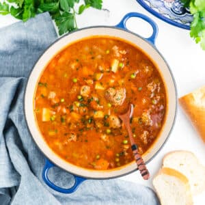 A large blue pot with a wooden spoon taking out some meatball stew.