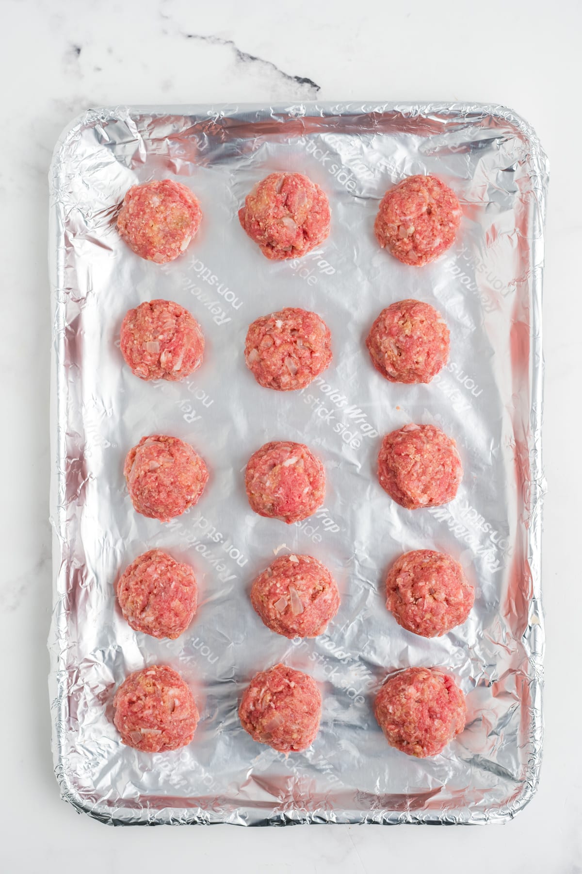 The meat mixture rolled into balls on a prepared baking sheet.