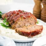 1 pound meatloaf sliced and served over mashed potatoes on a plate.