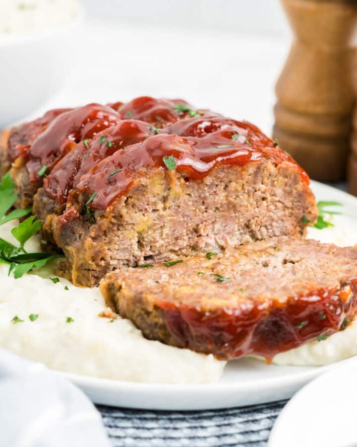 1 pound meatloaf sliced and served over mashed potatoes on a plate.
