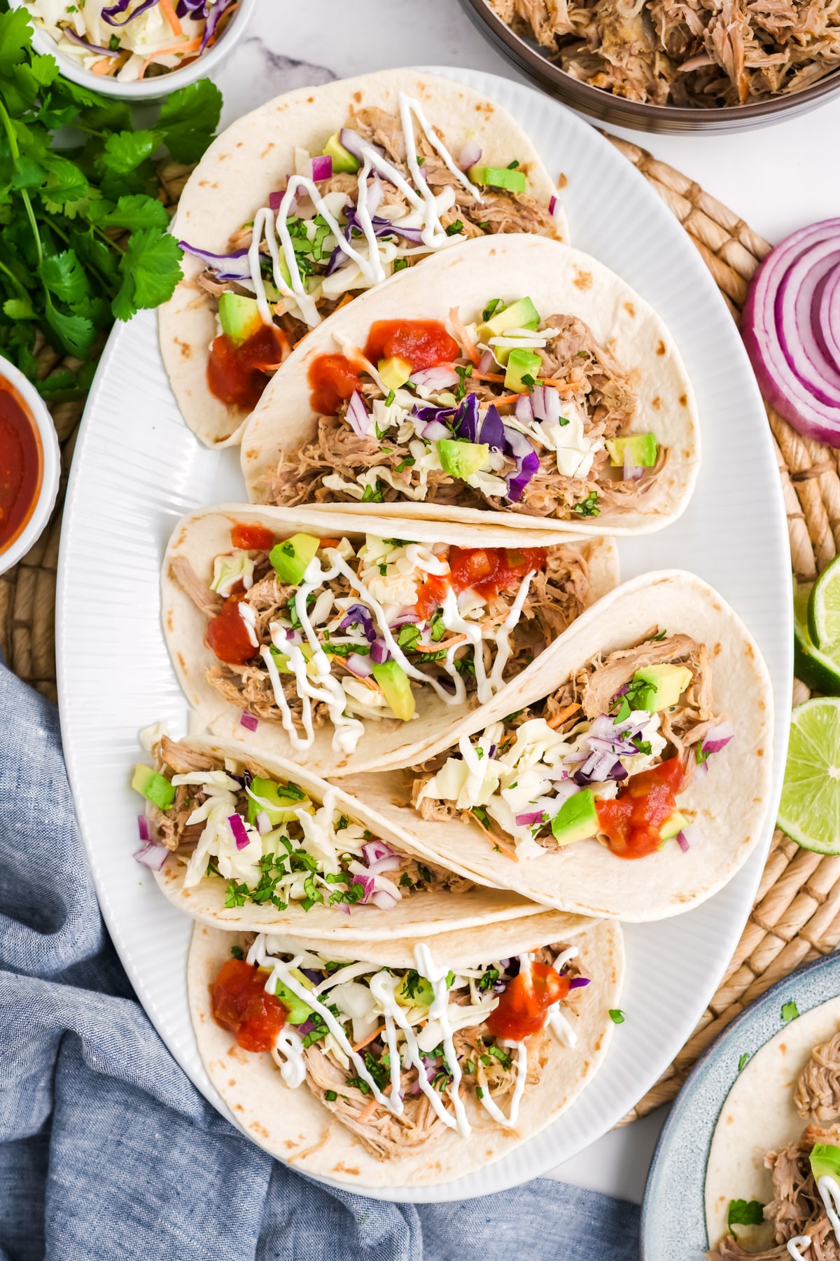 A plate filled with six pulled pork tacos with limes for garnish.