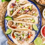A plate with pulled pork tacos with lime garnish.