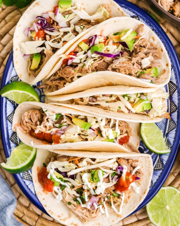 A plate with pulled pork tacos with lime garnish.