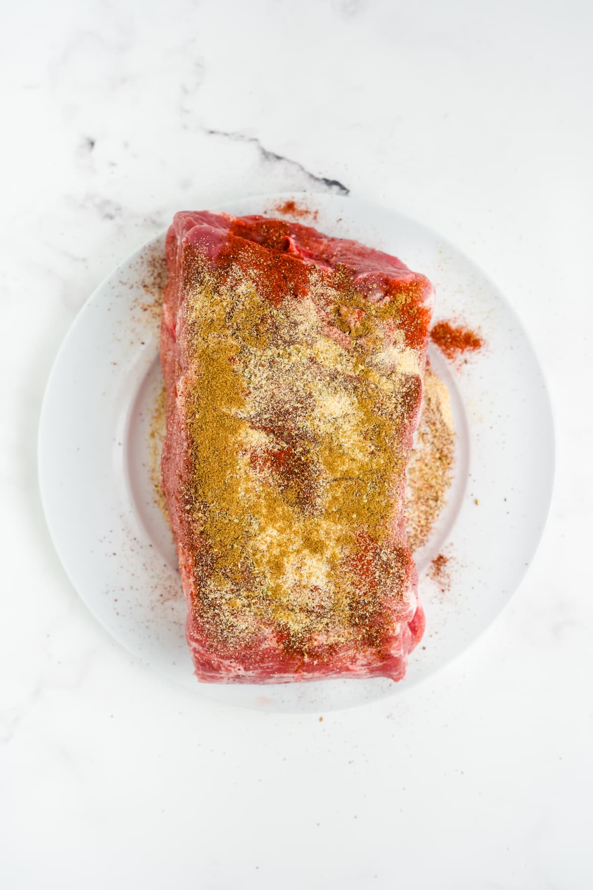 The pork on a plate with seasoning rubbed all over.