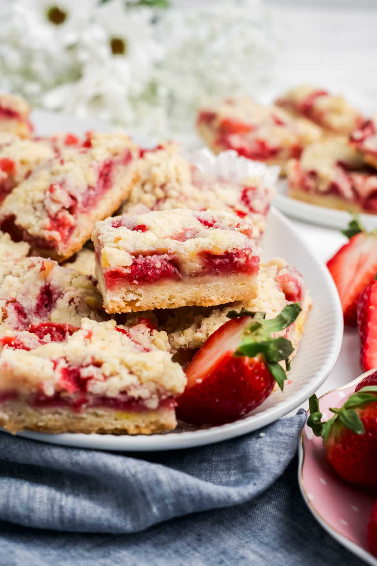 A plate filled with strawberry bars and garnished with fresh strawberry halves. 