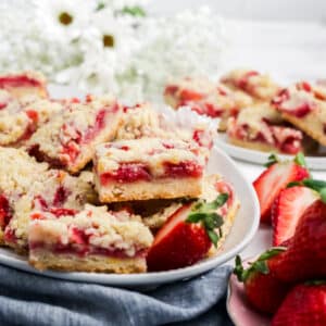Strawberry bars stacked on a plate and garnished with strawberry halves.