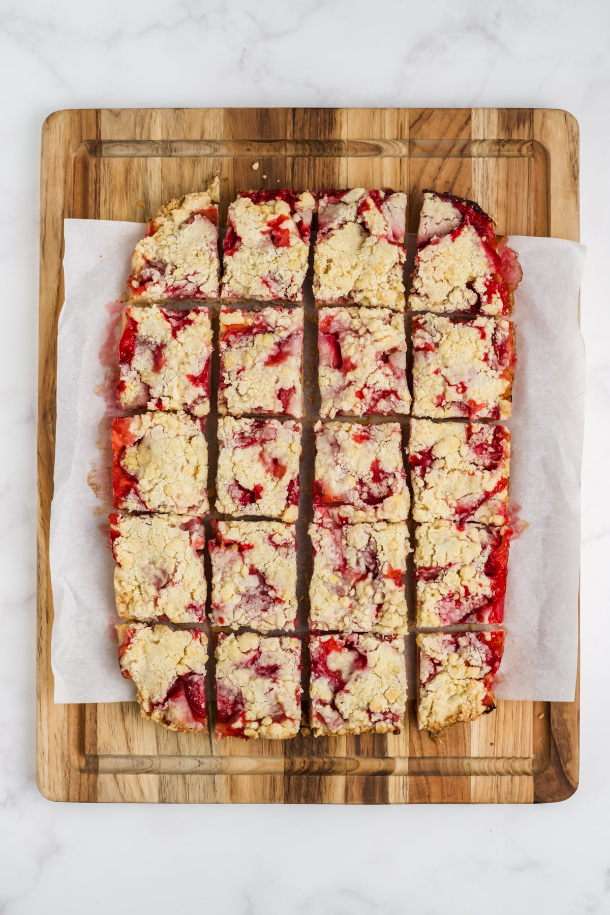 The strawberry bars cooled and sliced on a cutting board.