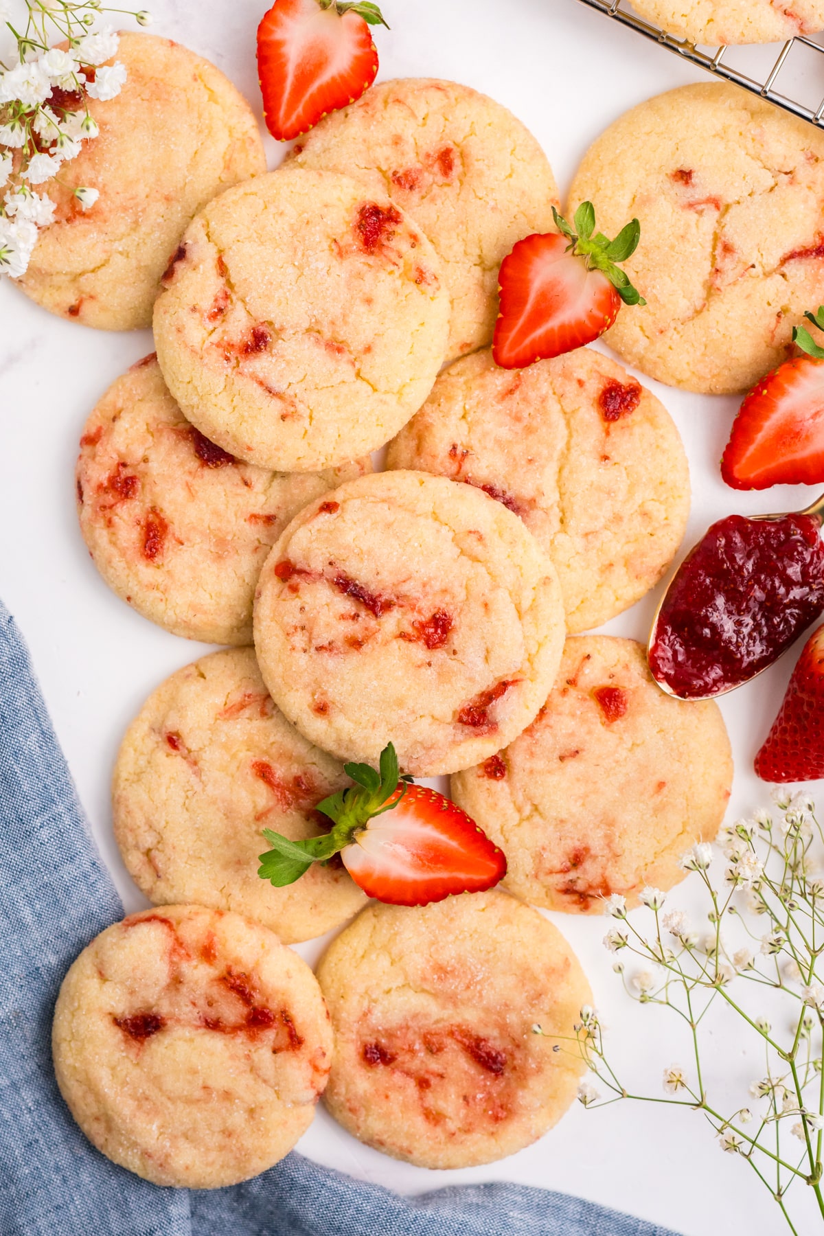 Strawberry sugar cookies stacked on a table with fresh berries and a spoonful of jam to the side. 