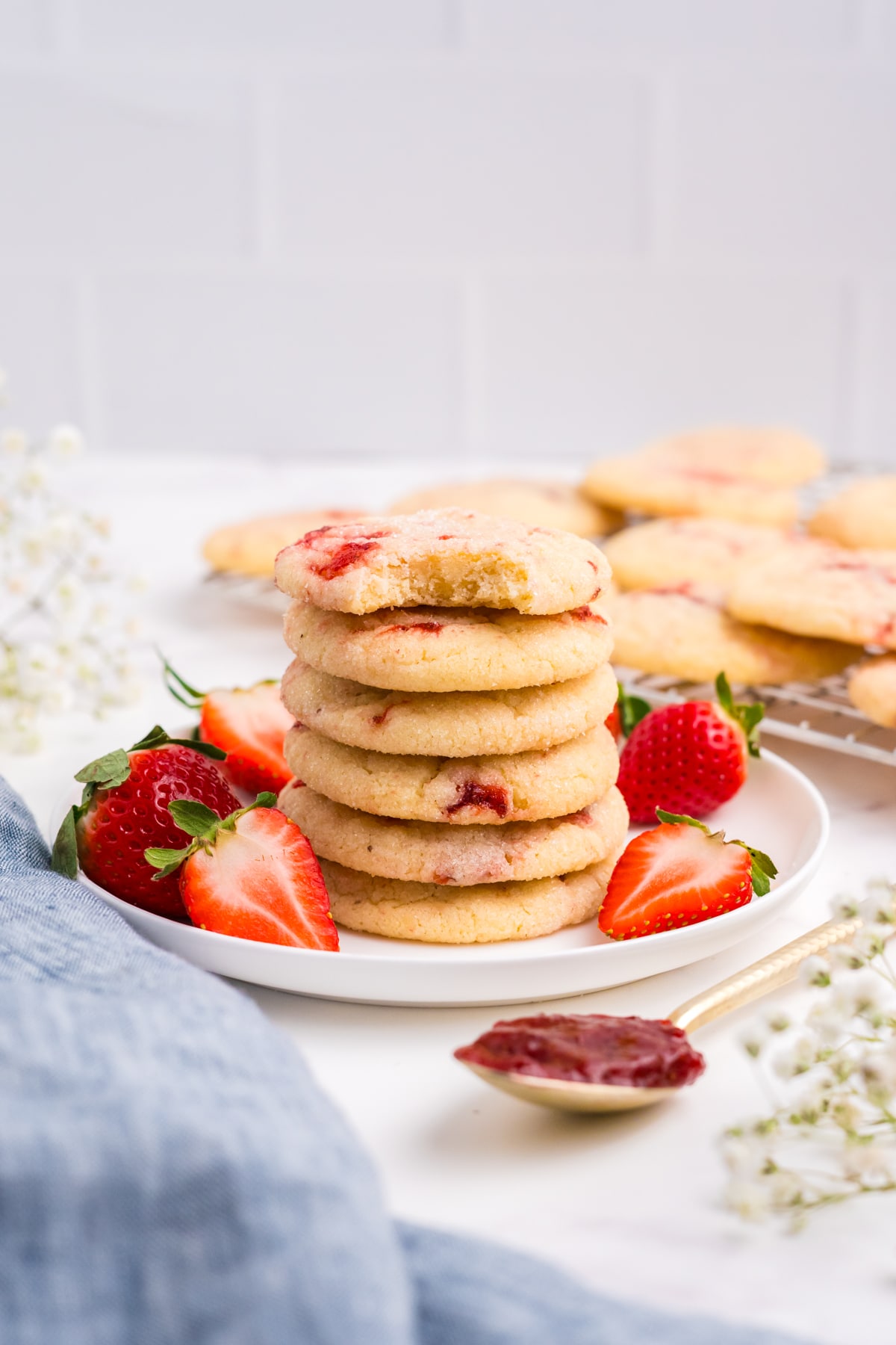 A pile of strawberry sugar cookies on a plate with a bite taken out of the top cookie.