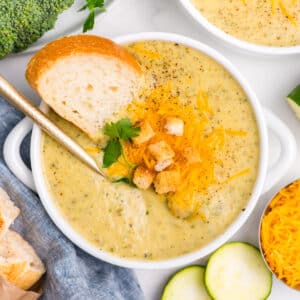 overhead image of white bowl of zucchini broccoli soup with a spoon in in it.