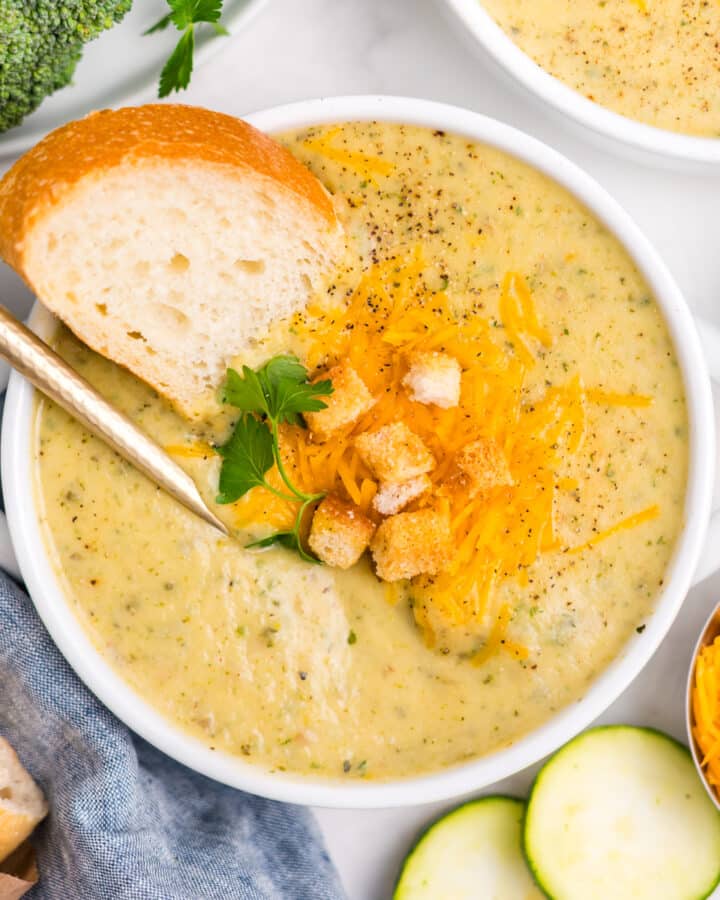 overhead image of white bowl of zucchini broccoli soup with a spoon in in it.